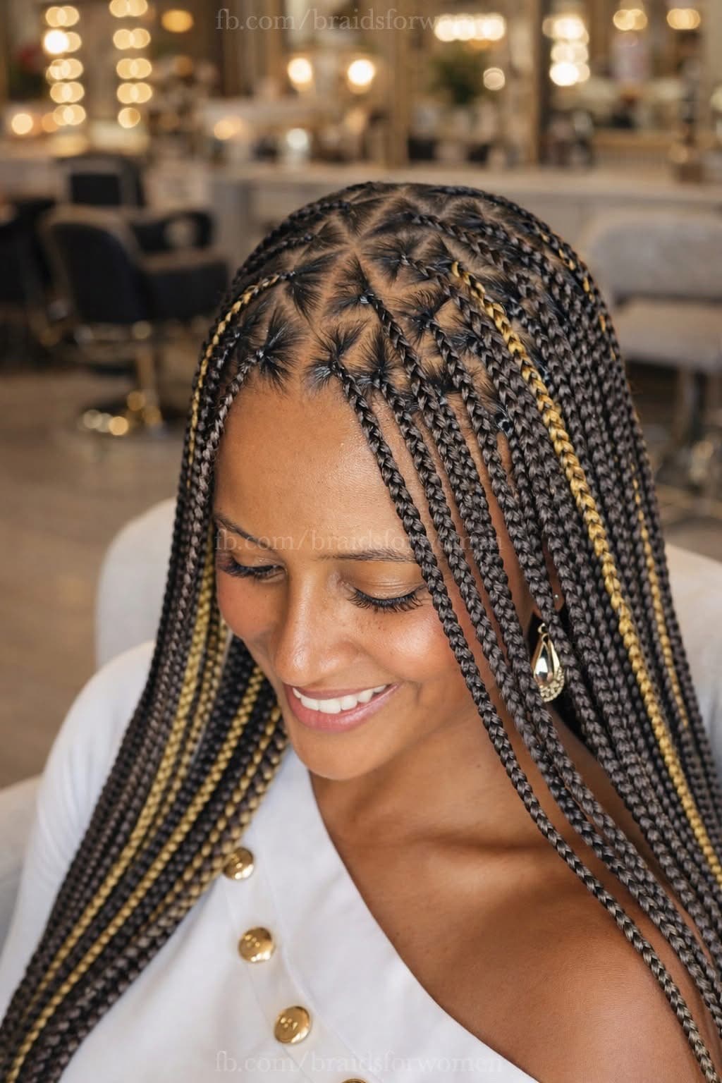 Smiling woman showcasing long dark box braids with triangle parts and golden highlight accents.